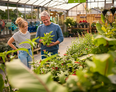 man and woman in greenhouse looking at plants discussing gardening tips